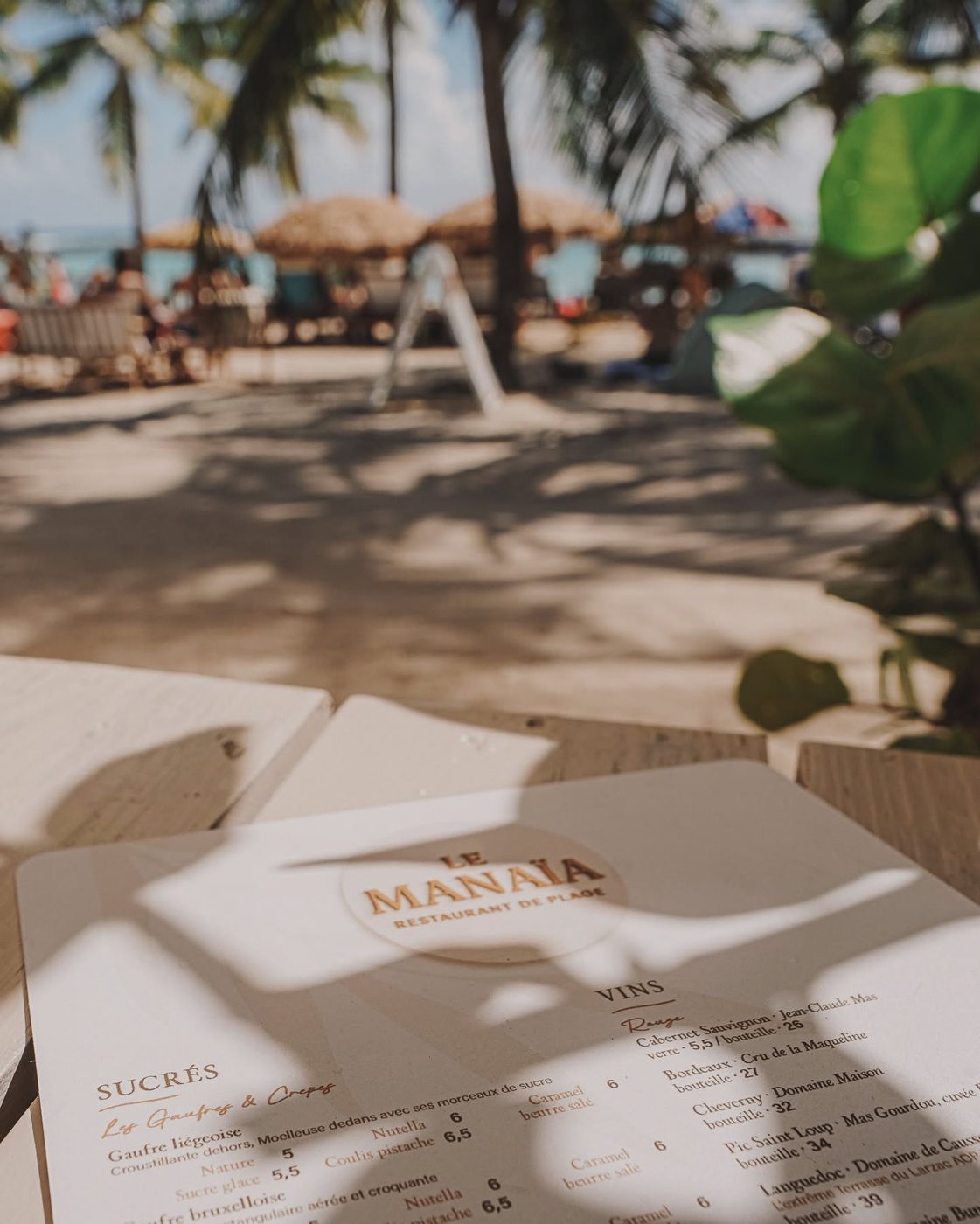 Carte du Manaïa posée sur une table de la terrasse, face aux parasols de paille et à la mer